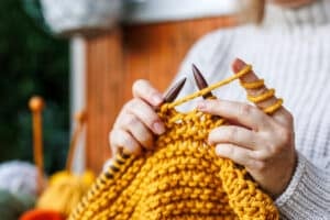 Knitting with wool. Woman in woolen sweater knits warm clothing of yellow yarn